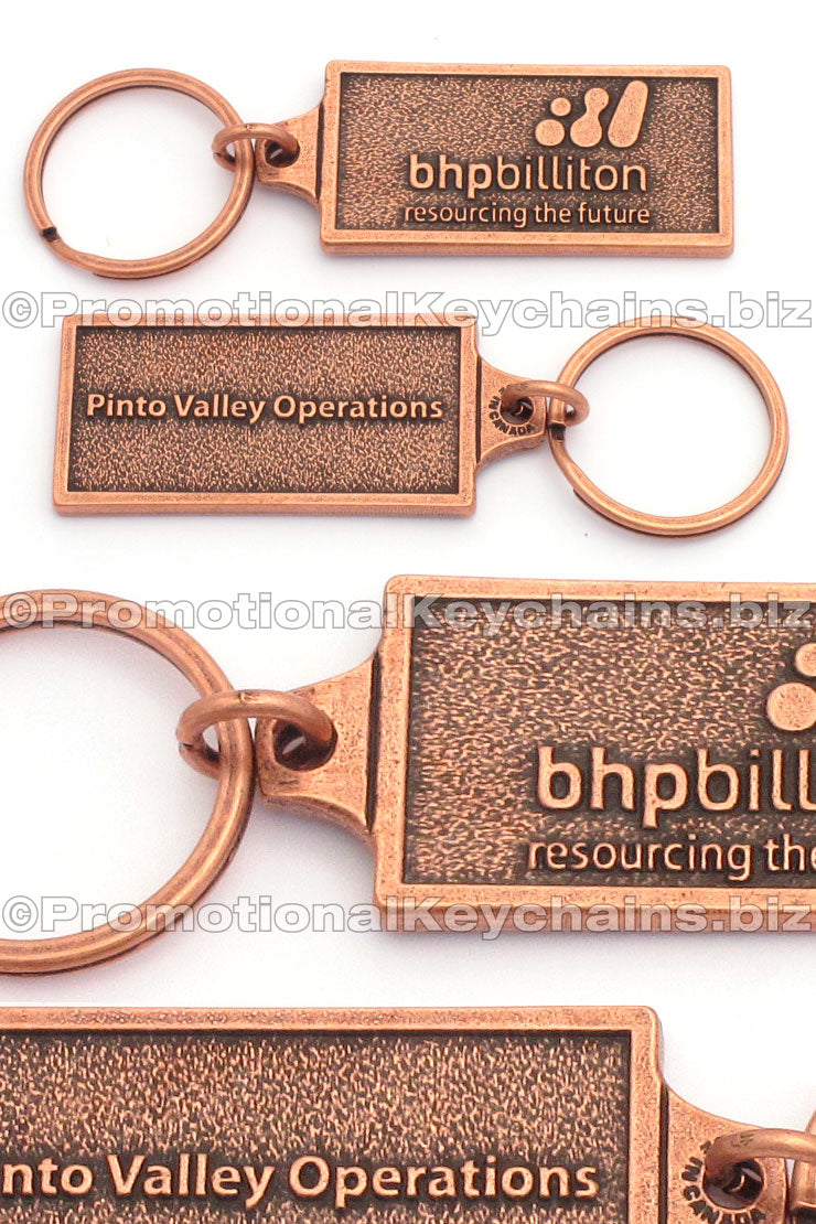 Multiple photos of the same rectangular antique copper keychain. The front has the logo for BHPBilliton embossed, and the back has the text "Pinto Valley Operations" embossed.