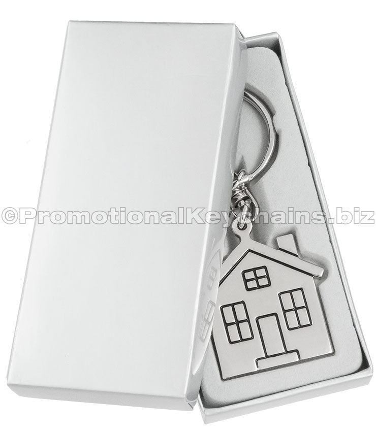 A polished metal house-shaped keychain displayed in a silver gift box.