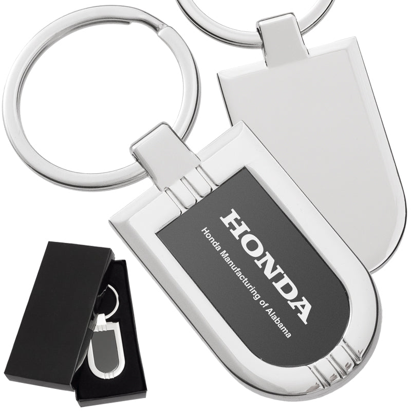 There are three images. On the left, a polished metal badge keychain featuring a black metal inlay displayed in a black gift box. On the right is the front and back of the same keychain with a logo clearly engraved in the center of the front side.