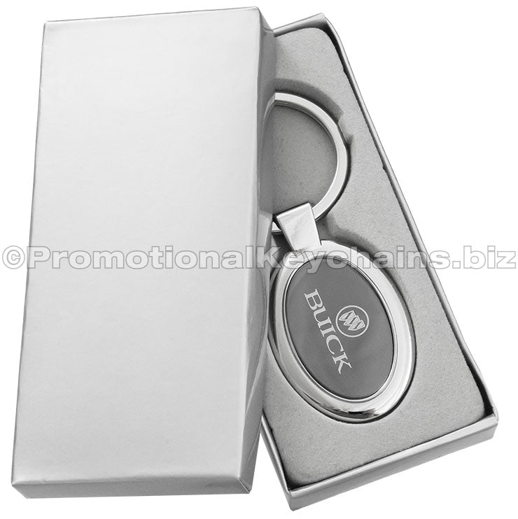 A polished metal ovular keychain featuring a black metal inlay engraved with the Buick logo displayed in a silver gift box.