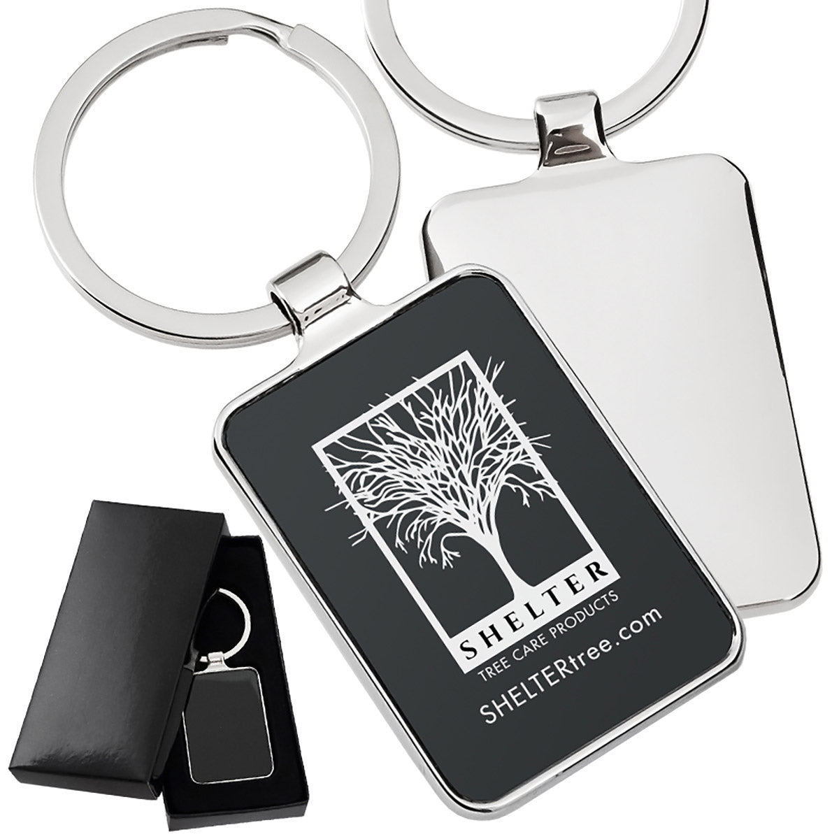 There are three images. On the left, a polished metal keychain featuring a black rectangular background displayed in a black gift box. On the right is the front and back same keychain with a logo clearly engraved in the center of the front side.