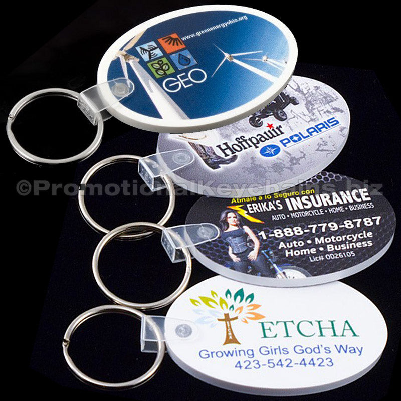 Collection of four oval vinyl material keychains with photorealistic branding on the front against a black background.