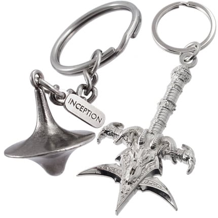 A photo of two different nickel plated three-dimensional keychains. On the left, a spinning top with an attached tag branded with the "INCEPTION" logo. On the right, a detailed, ornate mace design with dragon themed motifs.
