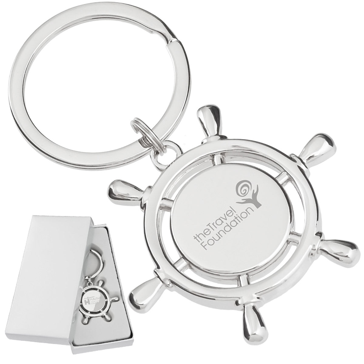 There are two images. On the left, a polished metal keychain that is shaped like a ship's wheel and laser engraved in the center. It is displayed in a silver gift box. On the right is the same keychain with a logo clearly engraved in the center.