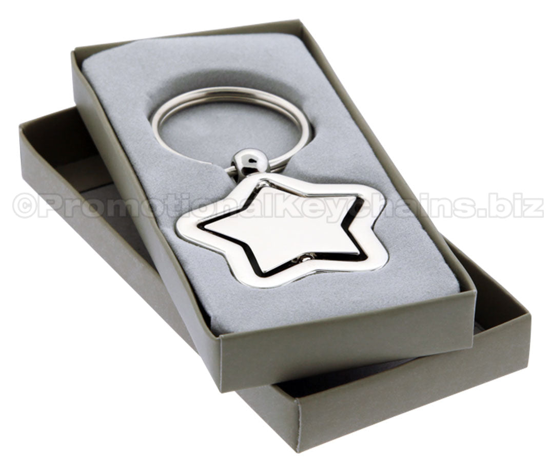 A polished metal star-shaped keychain with a spinning center. It is displayed in a grey gift box.