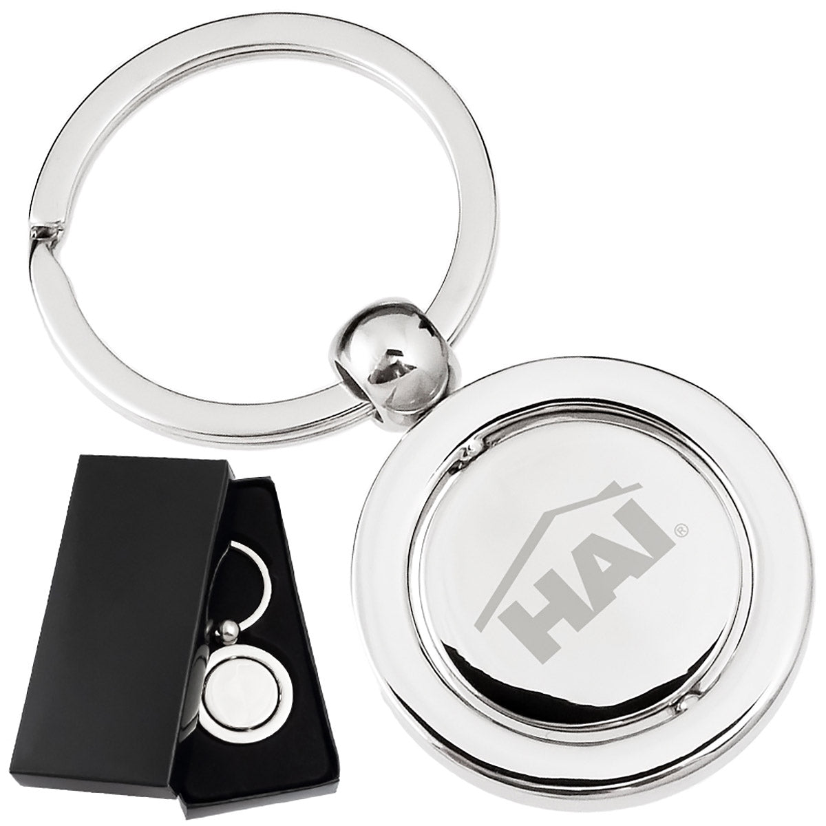 There are two images. On the left, a polished keychain featuring a round spinning disc in the center, displayed in a black gift box. On the right is the same keychain with a logo clearly engraved in the center.