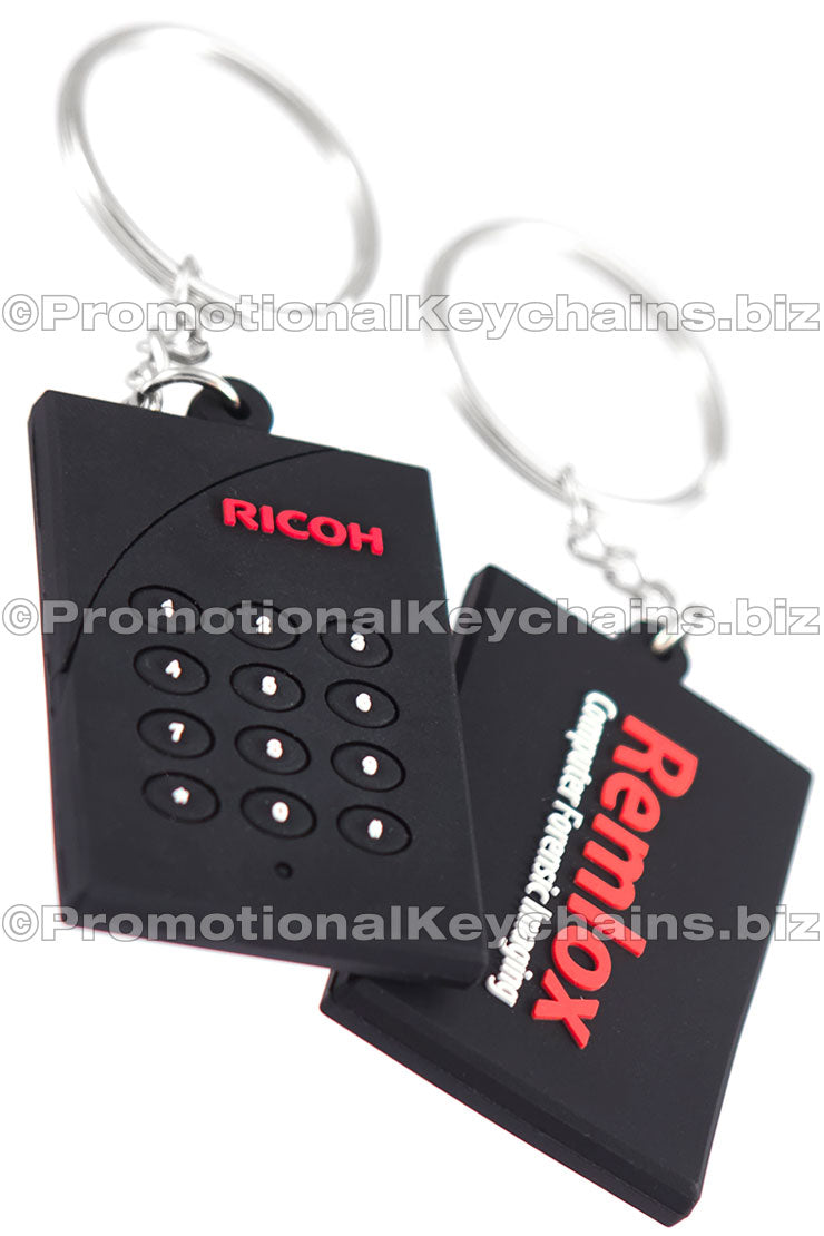 Both sides of a black 3D PVC keychain shaped like a keypad with "RICOH" branding in red. On the back, the "Remlox" logo is featured in red and white.