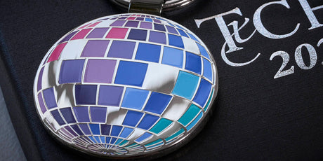 Front of custom made class year keychain in the shape of a disco ball, arranged on top of a custom box with printed logo. 