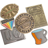 Layered image of antiqued lapel pins showing different colors and shapes.  Platings shown antiqued gold, brass and nickel. Some designs have enamel colors, blues, greens and oranges. 