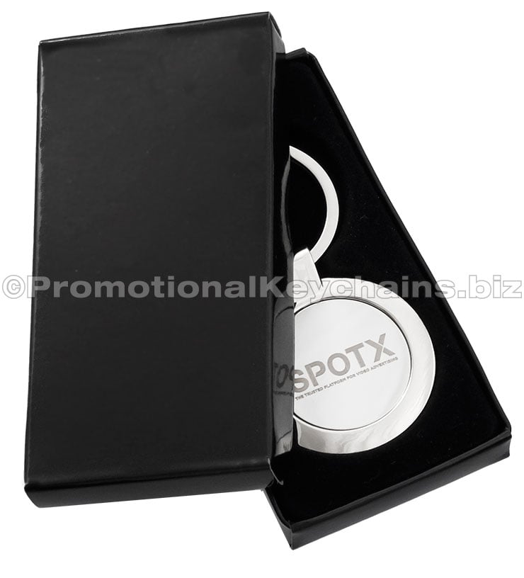 A polished circular metal keychain featuring an engraving and displayed in a black gift box.