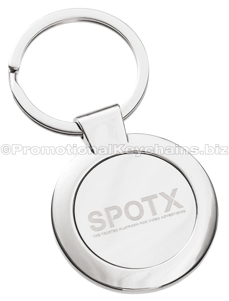 A polished, circular metal keychain featuring the "SPOTX" logo engraved in the center.