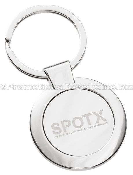 A polished, circular metal keychain featuring the "SPOTX" logo engraved in the center.