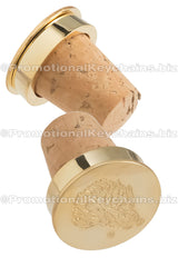 Two wine corks with polished gold metal tops, featuring an artistic boar head design die struck into the surface.