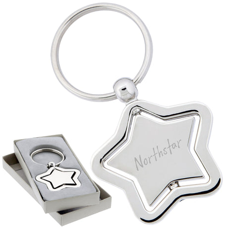There are two images. On the left, a polished metal star-shaped keychain with a spinning center. It is displayed in a grey gift box. On the right is the same keychain with a logo clearly engraved in the center.