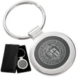 There are two images. On the left, a circular polished metal keychain featuring a black inlay displayed in a black gift box. On the right is the same keychain with a logo clearly engraved in the center.
