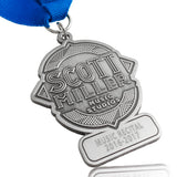 An antiqued nickel medal with blue ribbon, embossed with "Scott Miller Music Studios" in the center and "Music Recital 2016-2017" engraved on the bottom section.