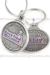Two angles of the same genuine pewter keychain, circular in shape. It features the logo for "Faith Farm Ministries" in purple and red enamel color.