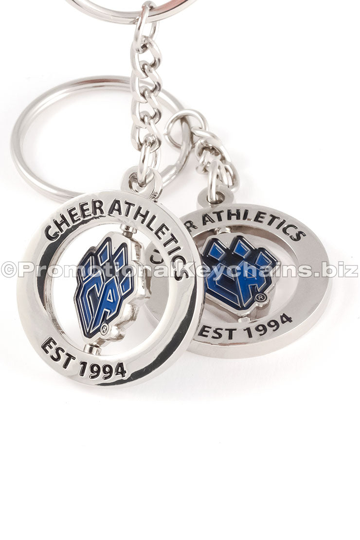 Two different angles of the same polished nickel spinning keychain featuring a "CA" logo shaped like a paw in blue enamel in the center and black text around the outer ring.