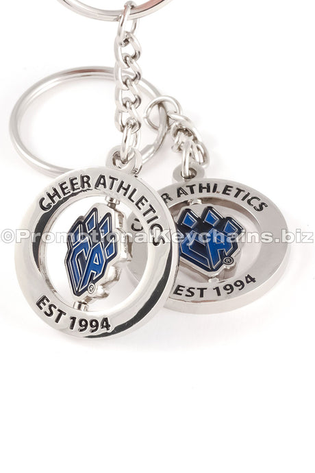 Two different angles of the same polished nickel spinning keychain featuring a "CA" logo shaped like a paw in blue enamel in the center and black text around the outer ring.