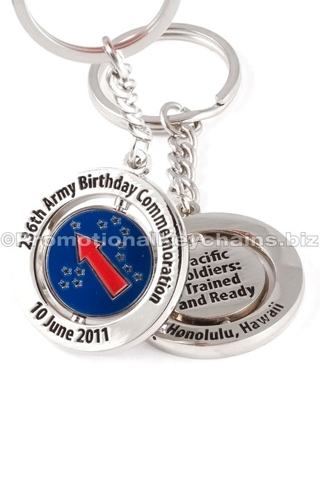 Both sides of a polished nickel spinning keychain. There is black text around the outer ring on both sides, with a center design that has a blue background and red arrow with stars.