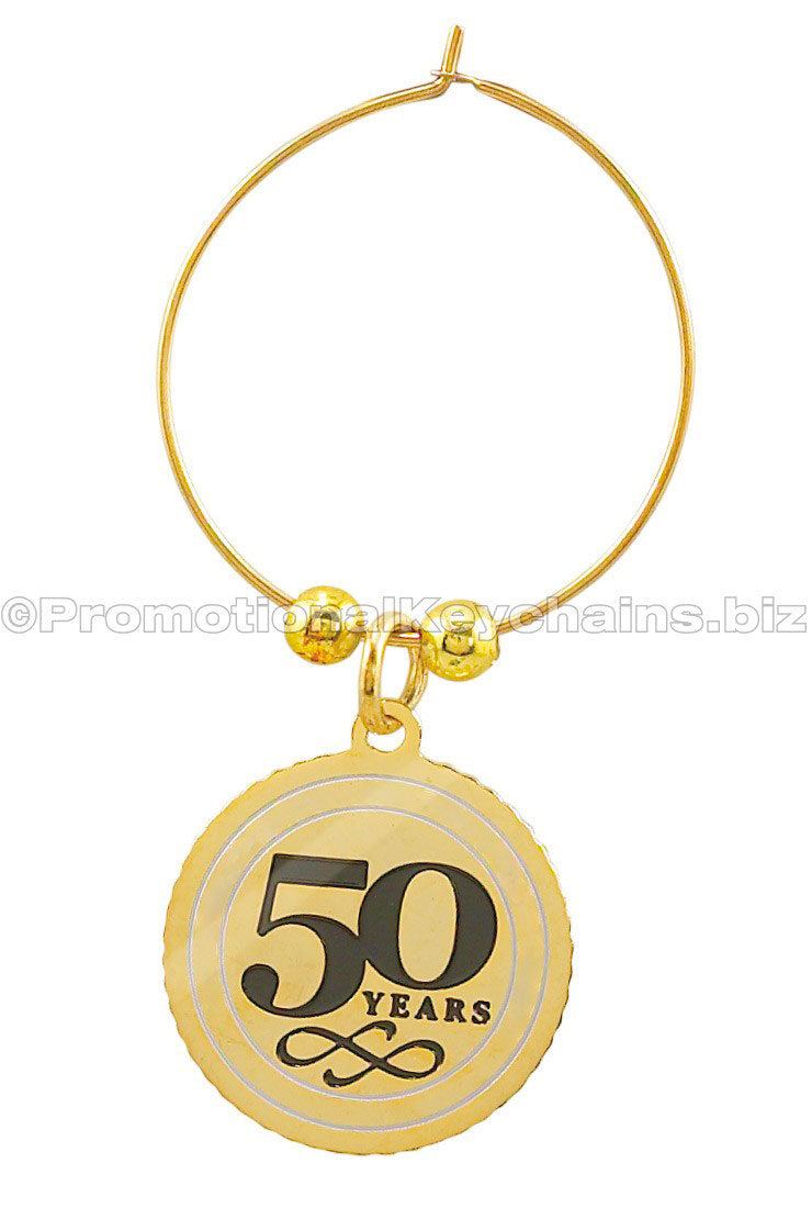 A polished brass wine charm featuring the text "50 years" in black enamel on the center of a medallion suspended from a golden hoop.