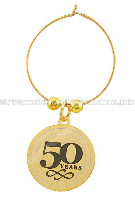 A polished brass wine charm featuring the text "50 years" in black enamel on the center of a medallion suspended from a golden hoop.