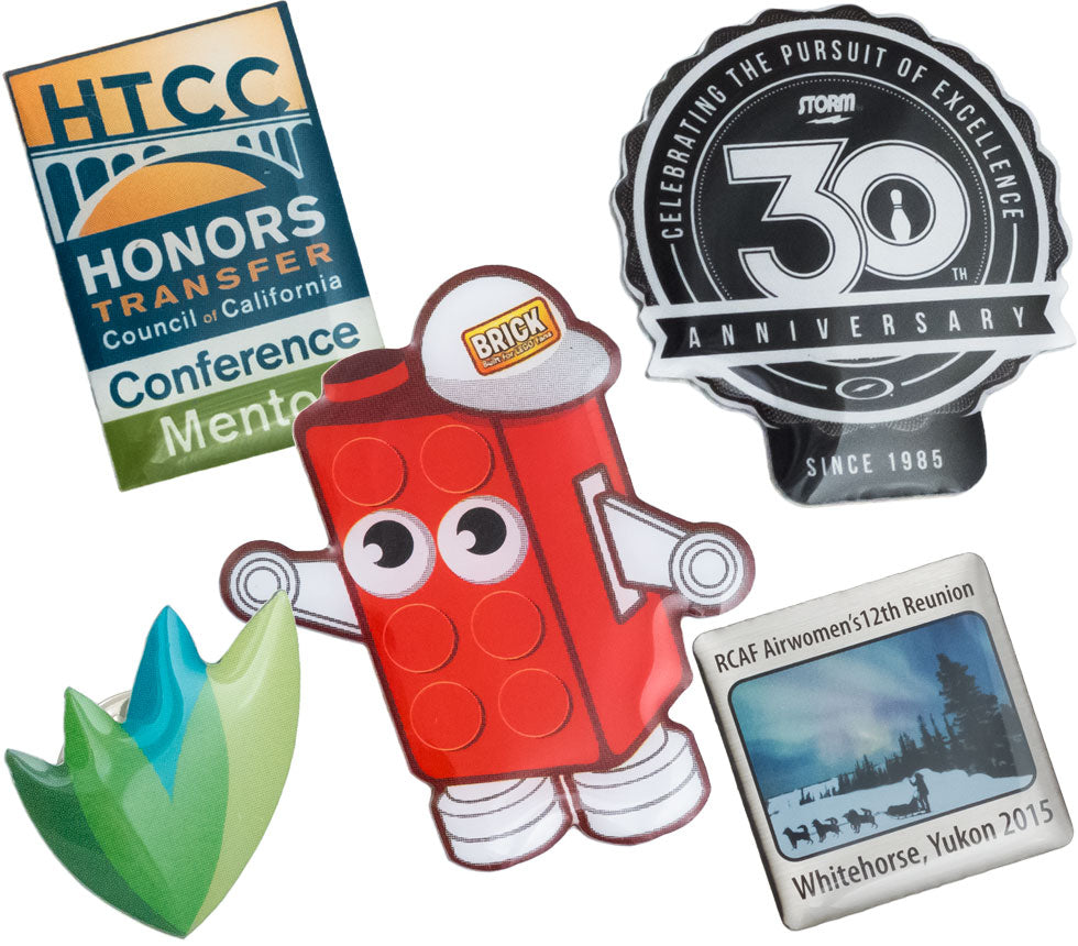 Layered image of Full Color Graphic Die Cut lapel pins showing different designs and shapes. Design include Lego brick with eyes and arms, 30th anniversary design and a leaf design. 