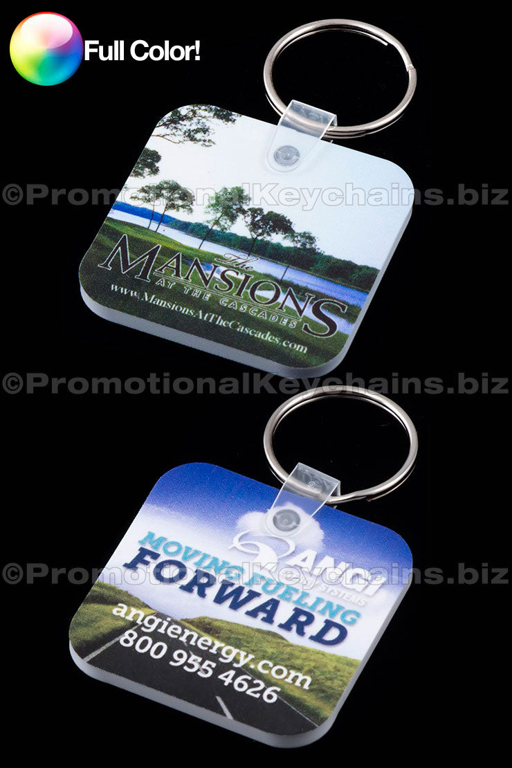 Pair of rounded square vinyl keychains with full color custom branding of Mansions at the Cascade and Moving Forward ANGI against a black background.