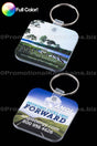 Pair of rounded square vinyl keychains with full color custom branding of Mansions at the Cascade and Moving Forward ANGI against a black background.