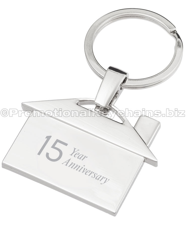 The back of a polished metal keychain that is shaped like a house, featuring an engraving of the text "15 Year Anniversary".