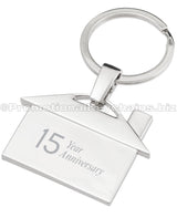 The back of a polished metal keychain that is shaped like a house, featuring an engraving of the text "15 Year Anniversary".