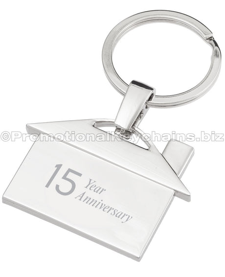 The back of a polished metal keychain that is shaped like a house, featuring an engraving of the text "15 Year Anniversary".