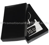 A polished metal house-shaped keychain featuring a '15 Year Anniversary" engraving, displayed in a black gift box.