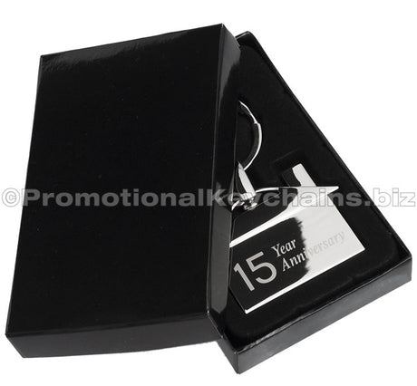 A polished metal house-shaped keychain featuring a '15 Year Anniversary" engraving, displayed in a black gift box.