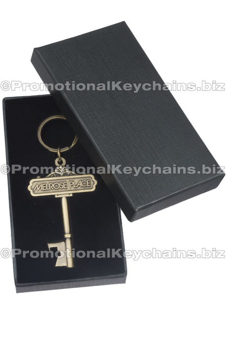 Antiqued gold key shaped bottle opener inside custom black box. Image shows box lid half open. 