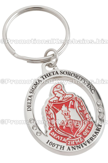 A circular polished nickel keychain featuring Delta Sigma Theta Sorority's emblem, embellished with red and black enamel color, commemorating its 100th anniversary.