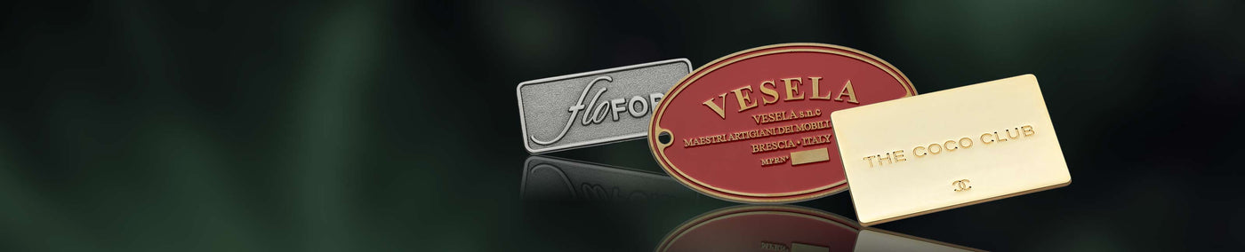 Three metal label plates with different branding on a dark reflective surface.