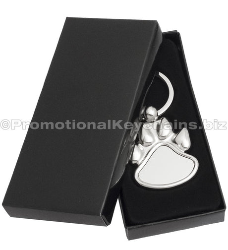 A polished metal paw-shaped keychain  displayed in a black gift box.