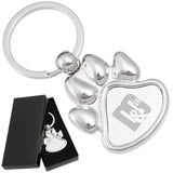There are two images. On the left, a polished metal paw-shaped keychain  displayed in a black gift box. On the right is the same keychain with a logo clearly engraved in the center.