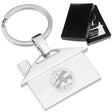 There are two images. On the right, a polished metal house-shaped keychain featuring a '15 Year Anniversary" engraving, displayed in a black gift box. On the left is the same keychain with a different logo clearly engraved in the center.